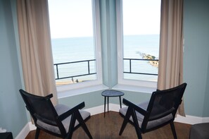 Une pièce avec vue sur la mer, deux chaises, une petite table et une fenêtre avec des rideaux.
