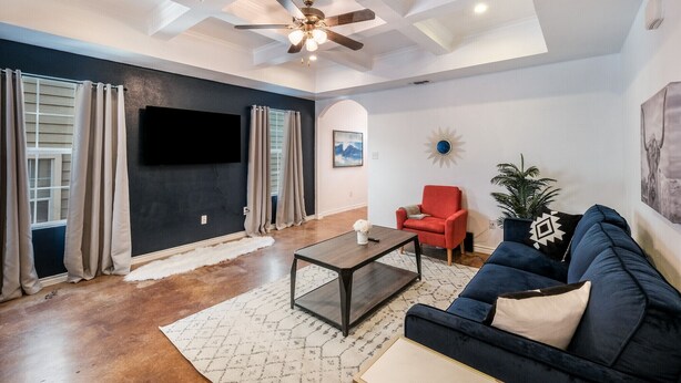 A living room with a dark wall, a ceiling fan, a mounted TV, a red chair, a dark blue sofa, and a white rug. - SP1  20% OFF New 3BR Home for Families or Large Groups 5-mins from Methodist (San Antonio)