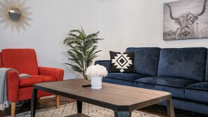 A living room with a red armchair, a blue sofa, a coffee table, a potted plant, and a wall-mounted mirror. - SP1  20% OFF New 3BR Home for Families or Large Groups 5-mins from Methodist (San Antonio)