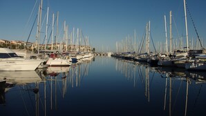 Un puerto deportivo con numerosos veleros amarrados, agua tranquila y edificios al fondo.