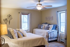 A bedroom with two beds, a ceiling fan, and large windows with curtains.