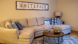 A living room with a beige sectional sofa, a coffee table, and a wall sign that reads "WHITEFACE".