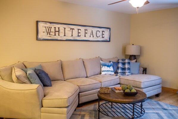 A living room with a beige sectional sofa, a coffee table, and a wall sign that reads "WHITEFACE".