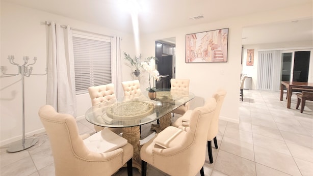 Un coin repas avec une table en verre entourée de six chaises rembourrées, un lustre et un tableau accroché au mur.