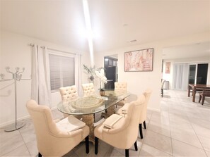 Un coin repas avec une table en verre entourée de six chaises rembourrées, un lustre et un tableau accroché au mur.