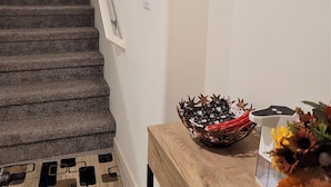 Un escalier recouvert de moquette menant à une porte, une console en bois ornée d’un vase décoratif et un vase rempli de fleurs.