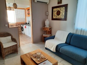 A living room with a blue sofa, wicker chairs, a wooden coffee table, and a kitchen area visible through an open doorway. - Oasis Suite, panoramic view of the Caribbean Sea with balcony! (Schoelcher)