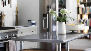 A modern kitchen with stainless steel appliances, a white island with stools, and a bookshelf in the background. - Healdsburg Homestead with Pool, Hot Tub and Tastings Included (Healdsburg)