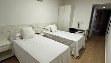 A hotel room with two single beds, a desk, a chair, a wardrobe, and an air conditioning unit.