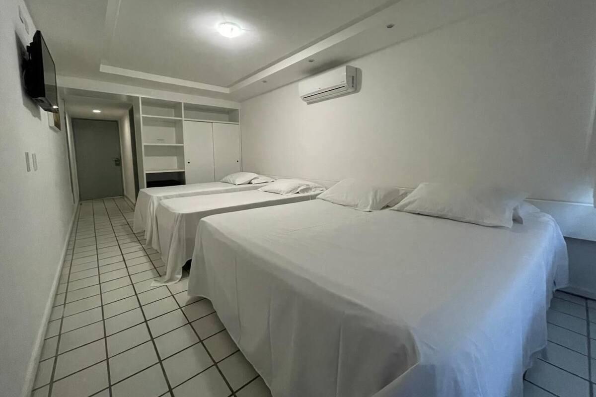 A hotel room with two beds, a TV, an air conditioning unit, and a tiled floor.