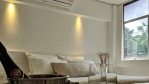 Una habitación moderna con una cama, una mesa con cubo para champán y copas, y un ventanal con vistas a árboles.