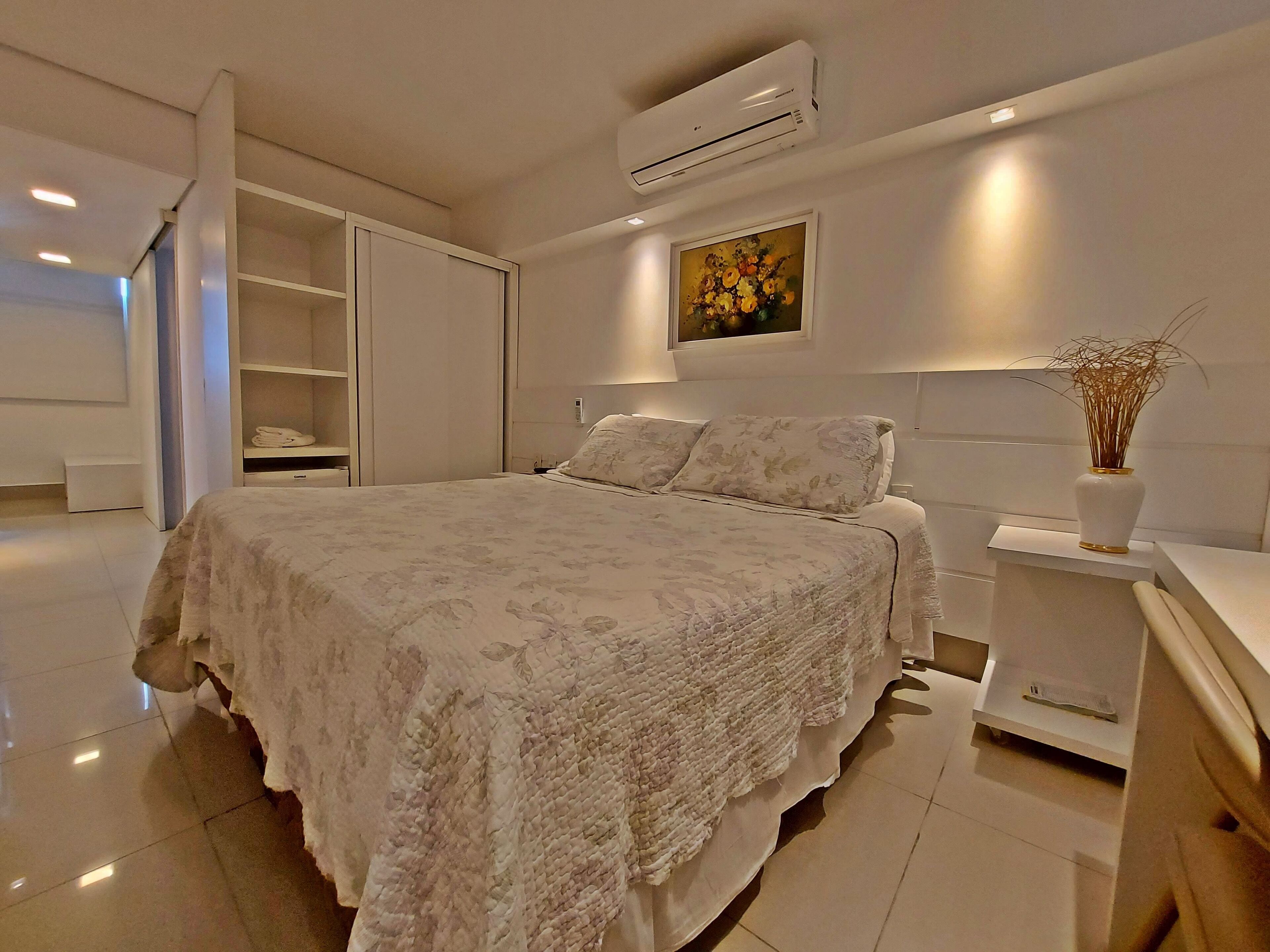 A modern bedroom with a large bed, a built-in wardrobe, and a bedside table with a vase.