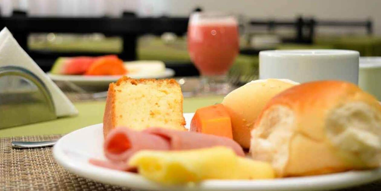 Un plato de desayuno con pan, jamón, queso y un vaso de jugo.