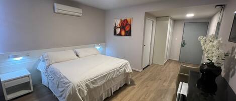 Un dormitorio con cama, mesitas de noche, un cuadro, una puerta y un florero con flores.