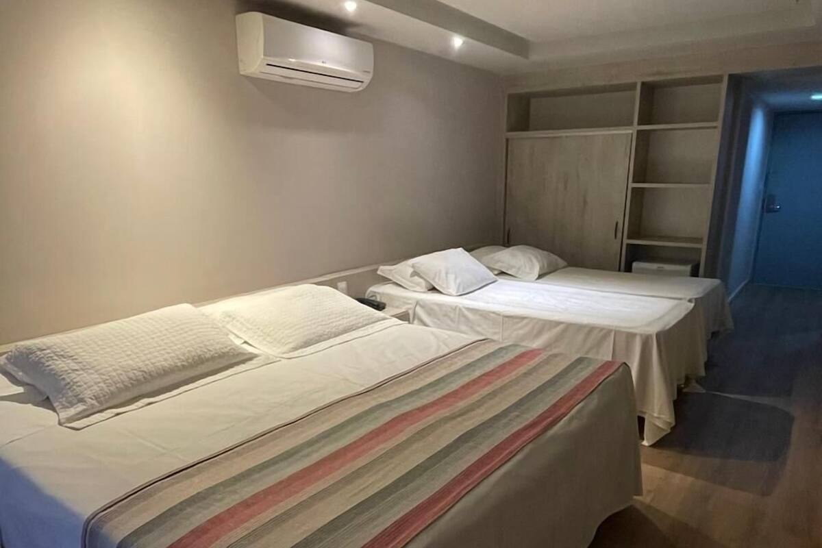 A hotel room with two single beds, a wardrobe, and a built-in air conditioning unit.