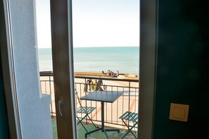 Un balcon avec une table et des chaises, donnant sur une plage où se trouvent des gens, et agrémenté d’une rambarde.
