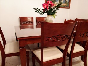 Una mesa de comedor con cuatro sillas, un jarrón con flores y un cuadro en la pared.