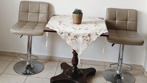 Comedor con dos sillas, una mesa con mantel floreado y varias estanterías con plantas y un original reloj en forma de cuchara.