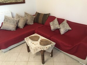 Un sofá rojo con cojines estampados, una mesita con mantel floral y un radiador al fondo.
