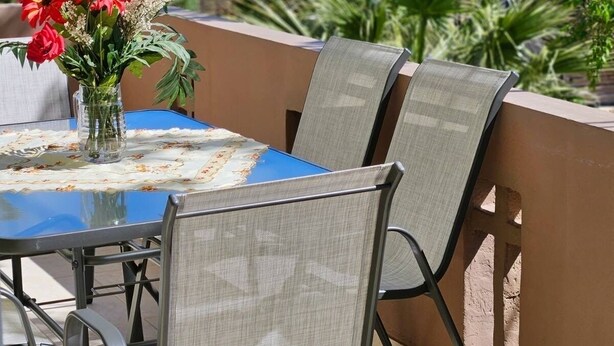 Un área de comedor al aire libre con una mesa y sillas, un florero con flores y vistas al mar y edificios en el fondo.