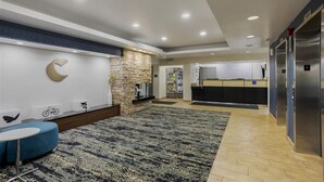 A modern hotel lobby with a stone accent wall, a seating area with a blue sofa, a kitchen area with stainless steel appliances, and an elevator. - Comfort Inn & Suites (Mount Laurel)