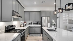 Una cocina moderna con armarios grises, electrodomésticos de acero inoxidable y encimera blanca.