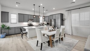 Una cocina moderna con armarios grises, una isla central, iluminación colgante y un comedor con mesa y sillas.