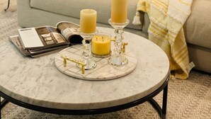 Una sala de estar con un sofá color crema, una mesa redonda de centro con velas y una revista.