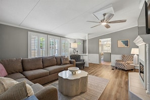 A living room with a sofa, armchairs, a coffee table, and a ceiling fan.