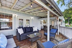 A covered outdoor seating area with wicker furniture, a glass table, and a white door.