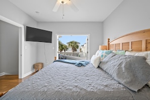 Relax in this serene bedroom with a large bed, TV, and ceiling fan, offering a view of palm trees and a balcony.