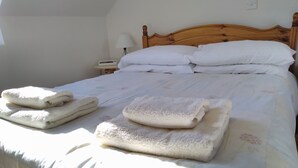 Un lit bien fait, avec du linge de lit blanc et des serviettes pliées, une tête de lit en bois et une table de chevet avec une lampe.