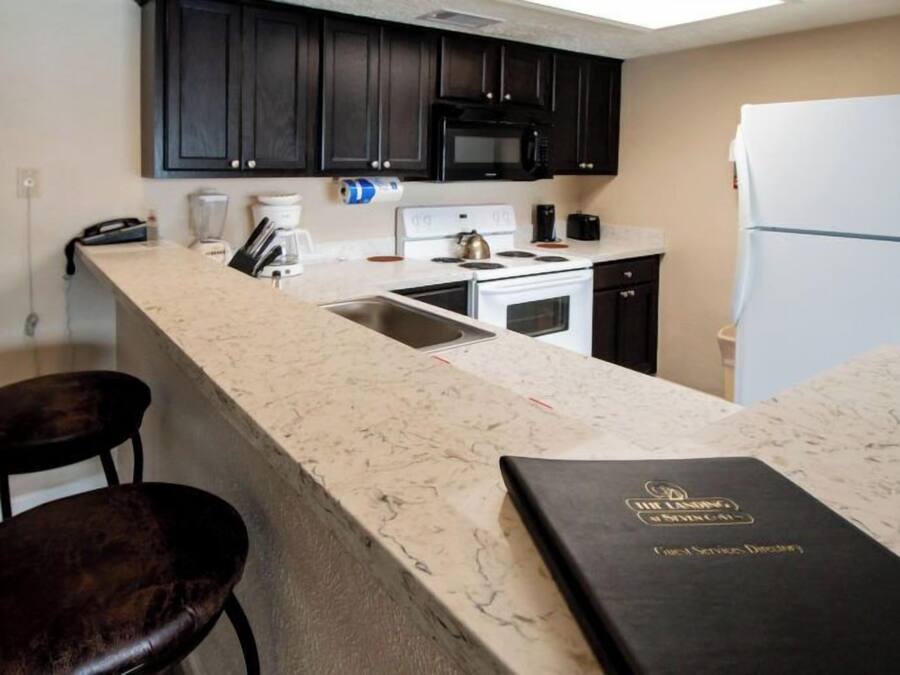 A kitchen with dark cabinets, a white stove, a microwave, and a refrigerator. There is a bar stool and a book on the counter.