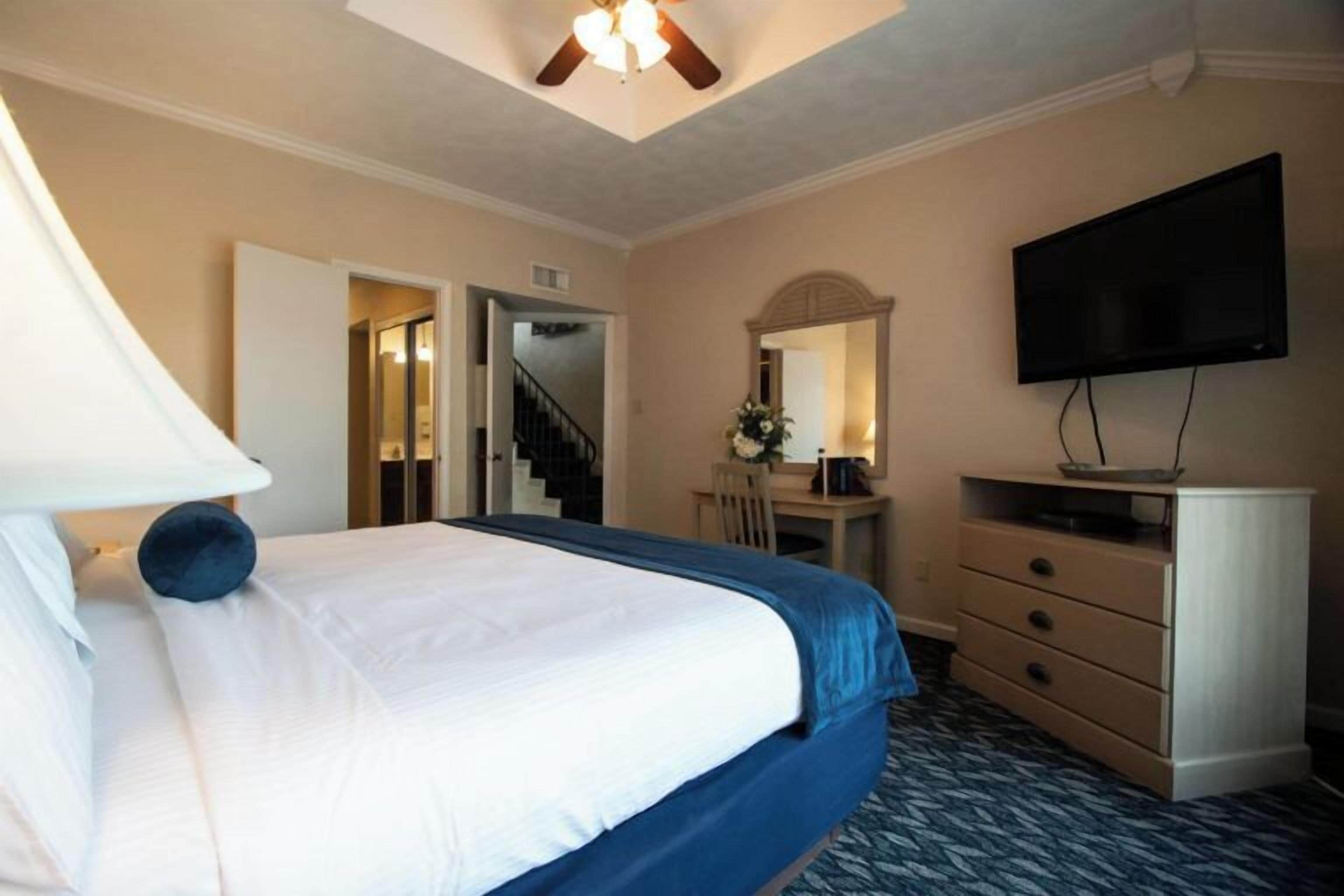A hotel room with a bed, a desk, a dresser, a TV, and a staircase leading to another room.