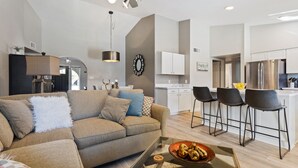 Een moderne woonkamer met een bank, een salontafel, en een keukenhoek met barstoelen.