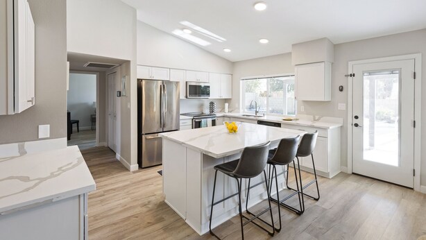 Een moderne keuken met witte kasten, roestvrijstalen apparatuur en een centraal eiland met barstoelen.