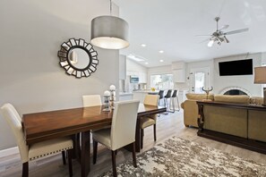Un salon moderne comprenant un coin repas, un canapé, un téléviseur fixé au mur et un ventilateur de plafond.