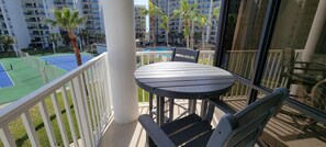 Enjoy a tranquil view of the tennis court and pool from this balcony, complete with a table and chairs.