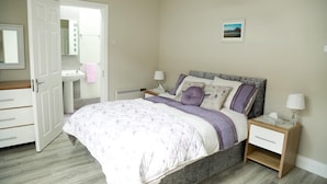 A bedroom with a bed, bedside tables, a nightstand, a dresser, a mirror, and a wall-mounted picture. - Killarney Town Center (Killarney)