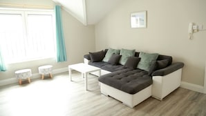 A modern living room with a sectional sofa, two side tables, and a large window with curtains. - Killarney Town Center (Killarney)