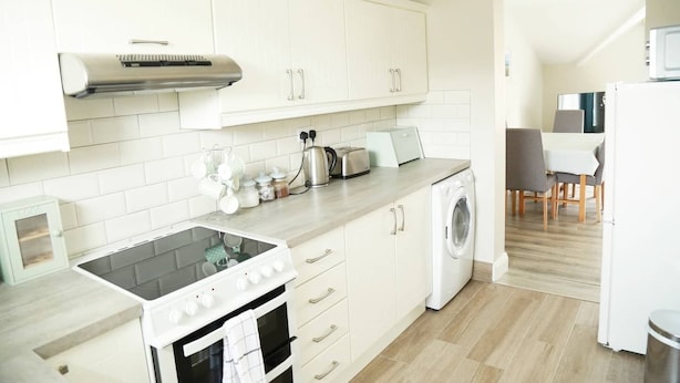 A modern kitchen with white cabinets, a built-in oven, a microwave, and a washing machine. - Killarney Town Center (Killarney)