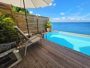 A wooden deck with a pool, lounge chairs, and a view of the ocean.