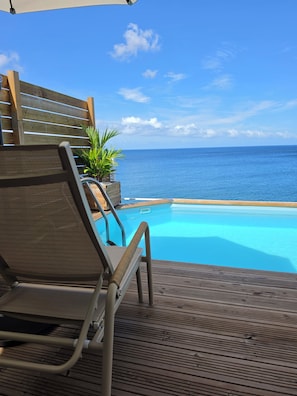 Una terraza de madera con piscina, sillas de descanso y vista al océano.