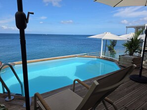 A pool with a wooden deck, lounge chairs, and umbrellas, overlooking the sea. - Balisier Suite, sea and pool view. (Schoelcher)