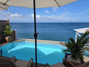 An infinity pool with a view of the ocean, wooden deck, and lounge chairs.