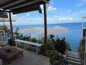 A terrace with outdoor seating, umbrellas, and a view of the sea.
