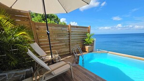 A wooden deck with a pool, lounge chairs, and a wooden fence. - Balisier Suite, sea and pool view. (Schoelcher)