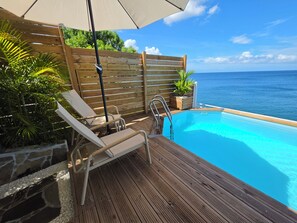 A wooden deck with a pool, lounge chairs, and a wooden fence.