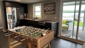 A modern kitchen with a foosball table, stainless steel appliances, and a large window overlooking a green landscape. - Perfect lake home for a family get away - Only 1 hour from metro (South Haven)