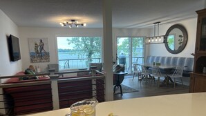 A modern kitchen with a large island, a dining area with a view of the outdoors, and a living space with a large window overlooking a body of water. - Perfect lake home for a family get away - Only 1 hour from metro (South Haven)